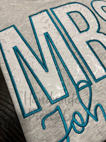 Embroidered text on a fabric with a focus on 'MRS' in teal thread.